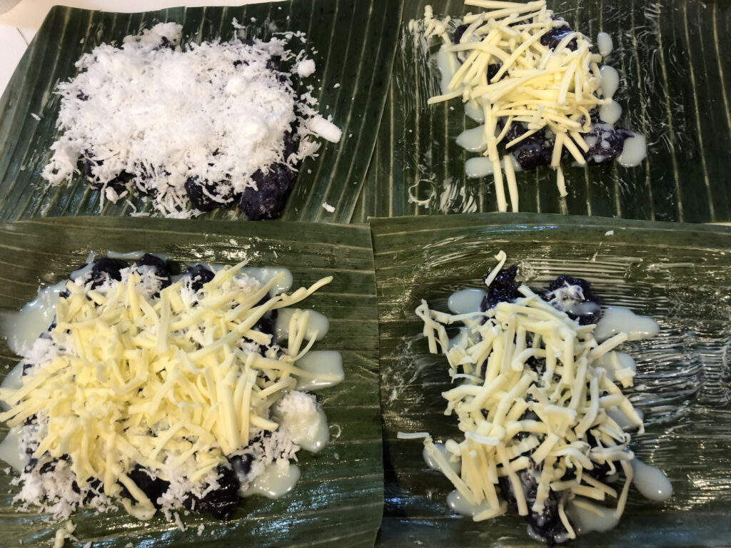 putobumbong. purple glitinous chewy rice cake. topped with grated coconut and sugar. or cheese with condensed milk