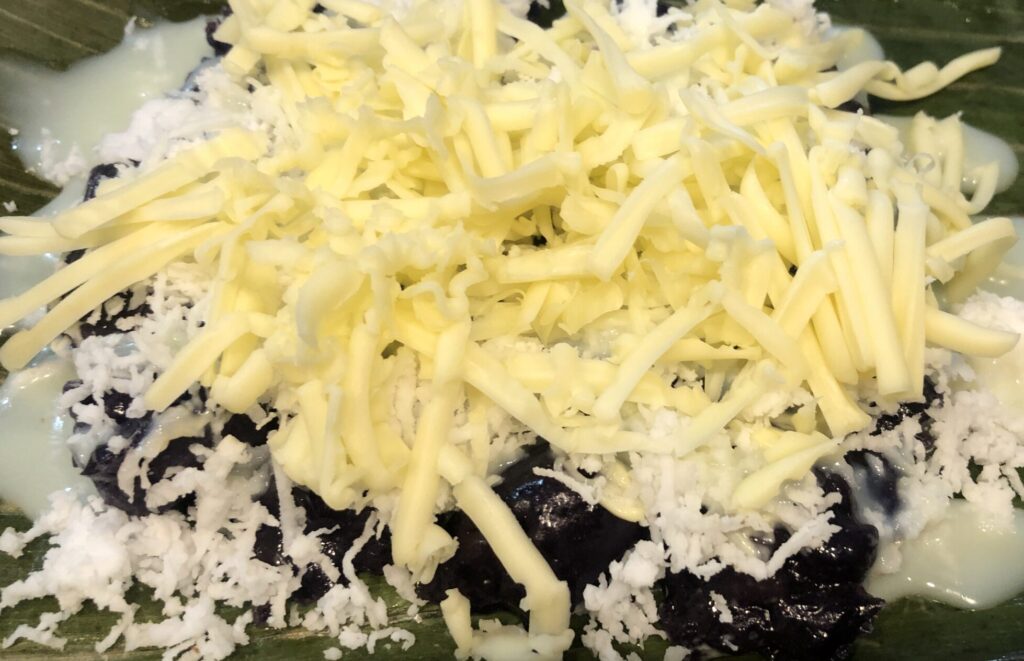 Puto Bumbong topped with grated coconut, sugar or condensed milk and cheese